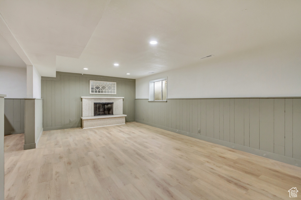 Basement with light wood-style floors, a wainscoted wall, a fireplace, and recessed lighting