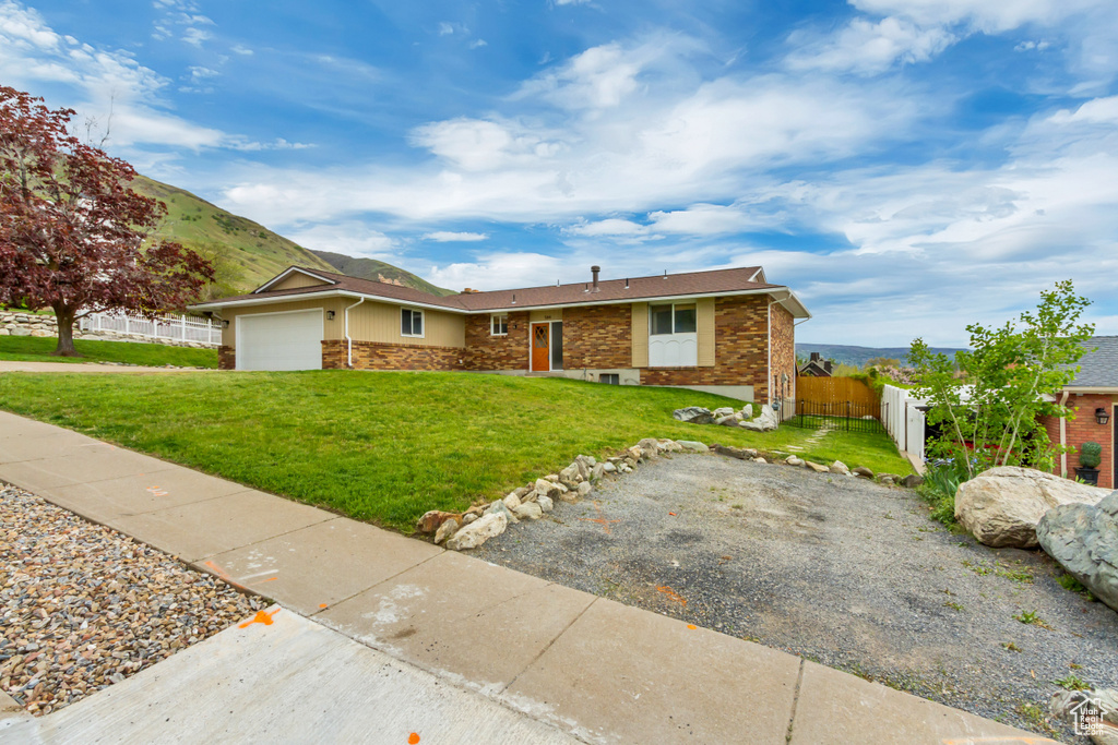 Ranch-style home with fence, an attached garage, stone siding, and a front yard