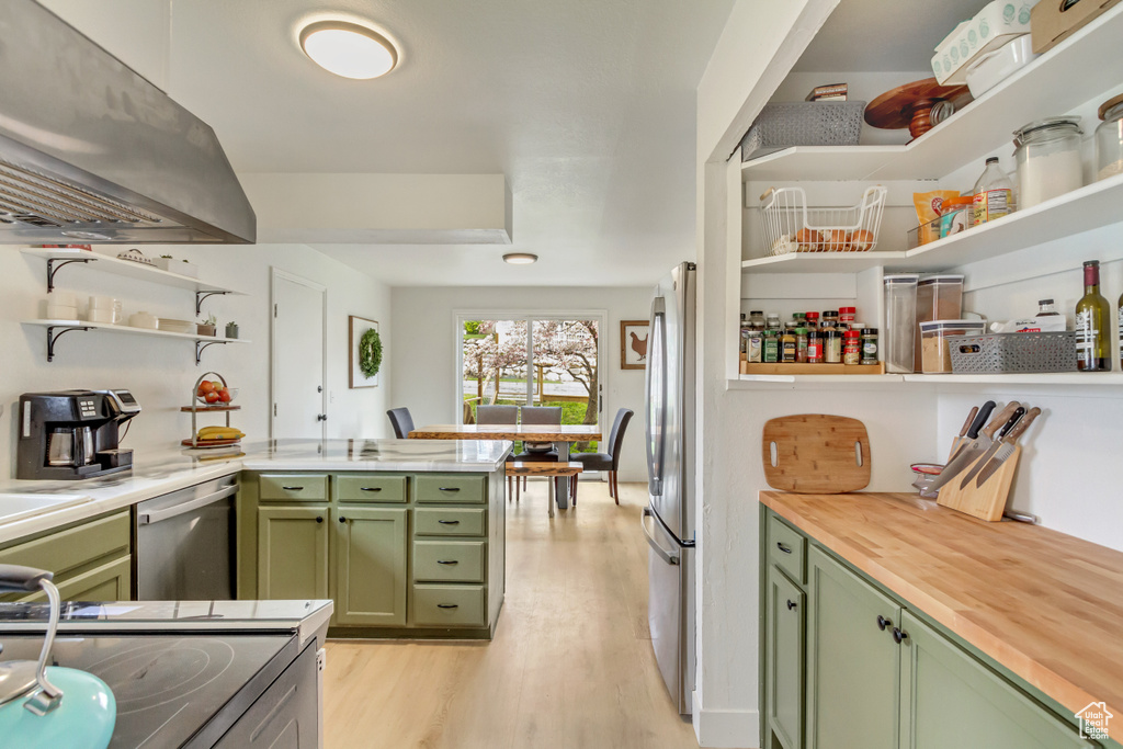 Kitchen with green cabinetry, open shelves, stainless steel appliances, range hood, and butcher block counters