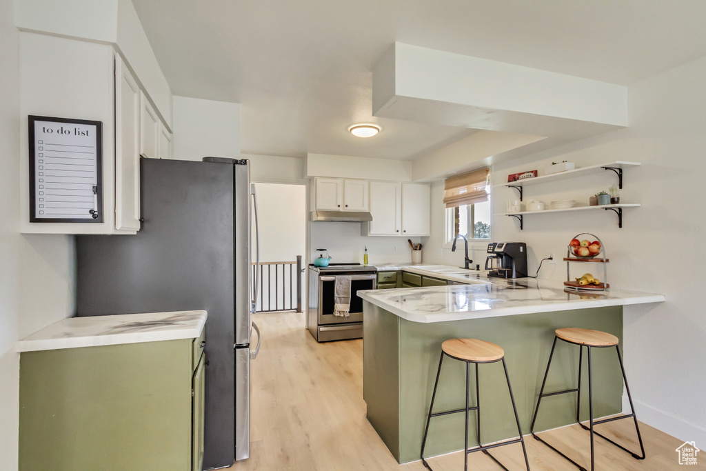 Kitchen with light countertops, stainless steel appliances, a peninsula, a kitchen bar, and under cabinet range hood