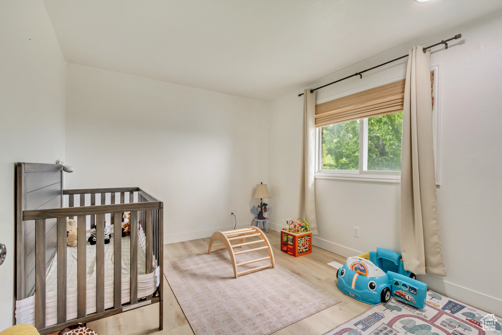 Bedroom with baseboards, a nursery area, and wood finished floors