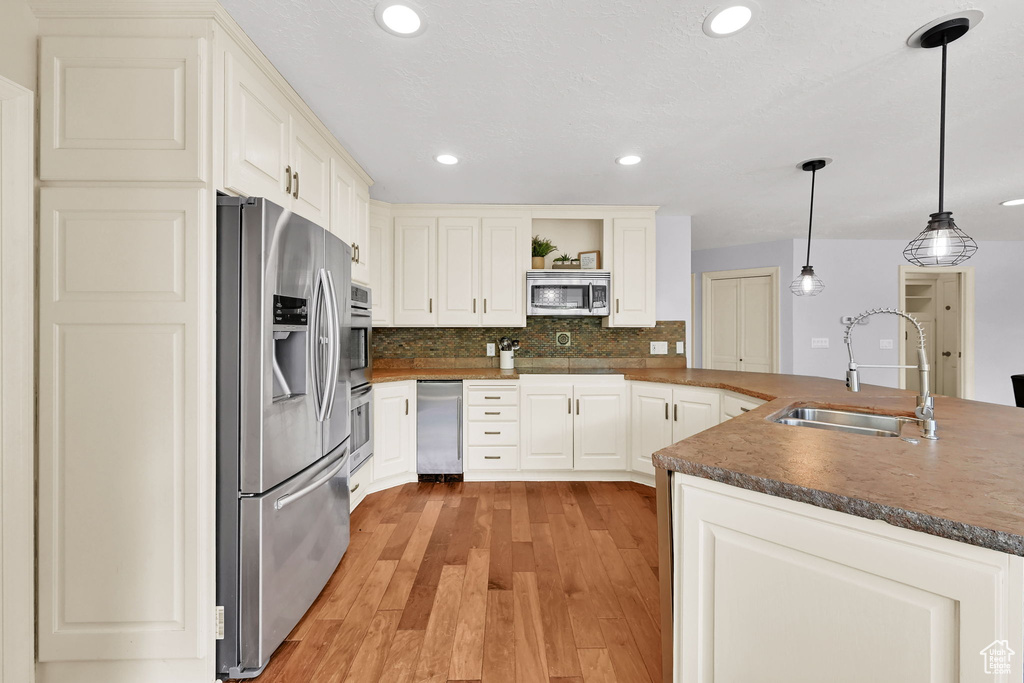 Kitchen with appliances with stainless steel finishes, dark countertops, open shelves, a sink, and light wood-style floors