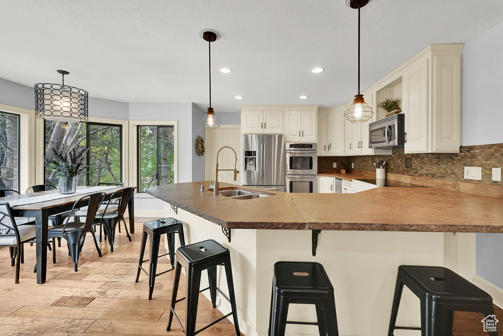 Kitchen with decorative backsplash, appliances with stainless steel finishes, a sink, light wood finished floors, and recessed lighting