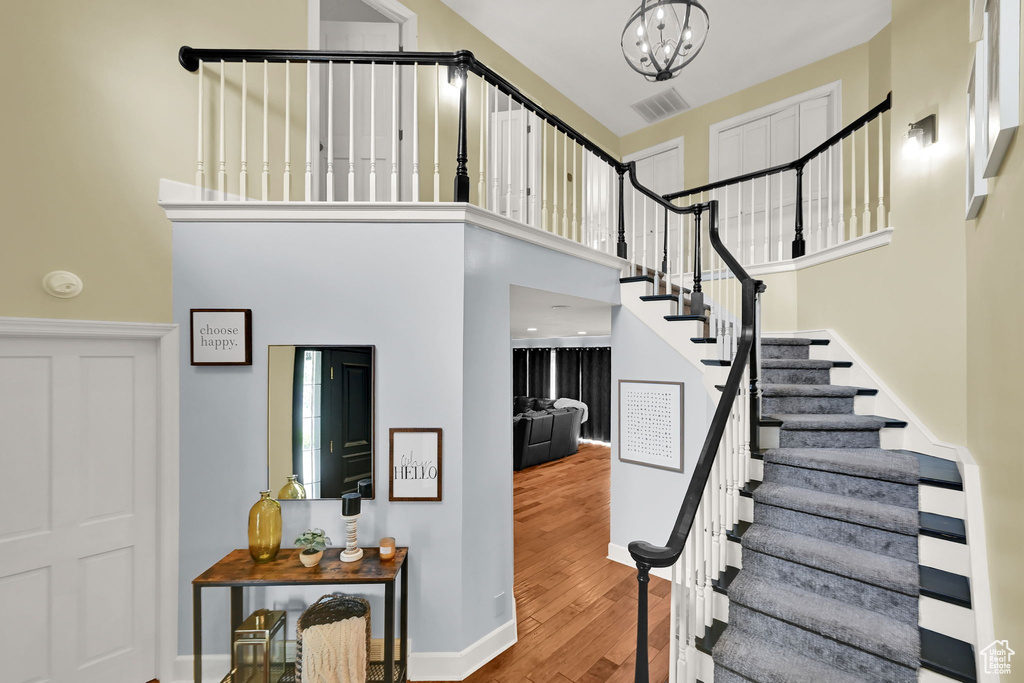 Stairs featuring visible vents, a towering ceiling, wood finished floors, baseboards, and a notable chandelier