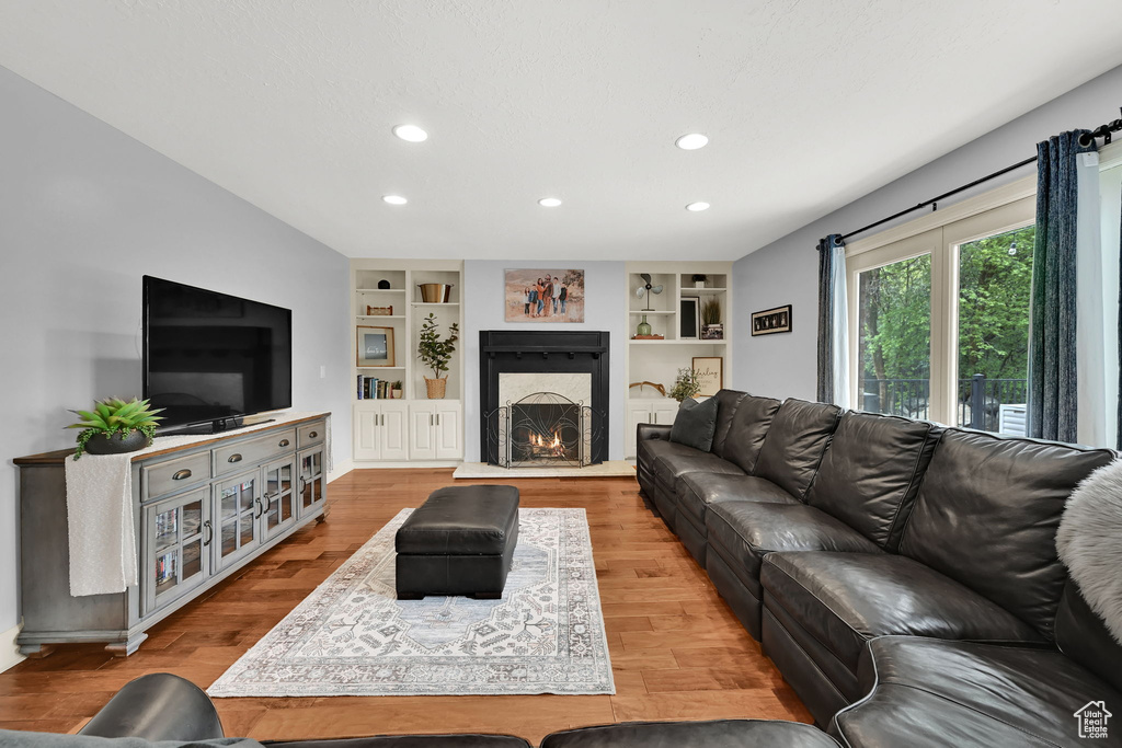 Living room featuring recessed lighting, a warm lit fireplace, built in features, and wood finished floors