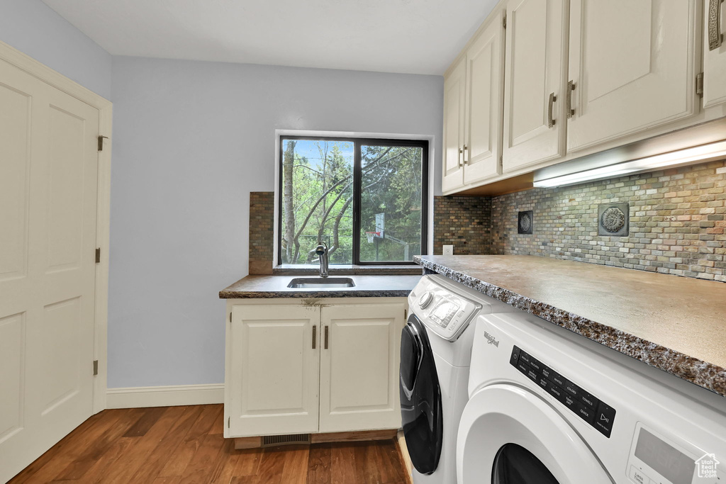 Washroom featuring cabinet space, dark wood-style flooring, a sink, baseboards, and washer and clothes dryer