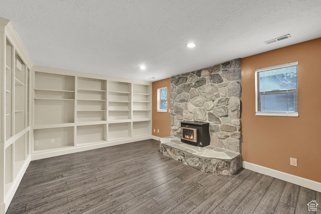 Unfurnished living room featuring baseboards, visible vents, a textured ceiling, and wood finished floors