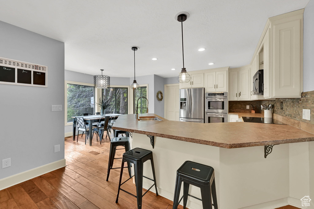 Kitchen with a peninsula, tasteful backsplash, a sink, light wood-style flooring, and stainless steel appliances