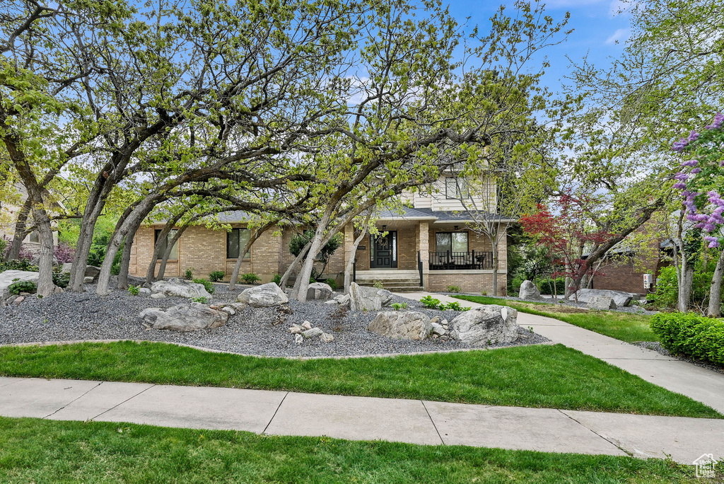 View of property hidden behind natural elements featuring covered porch, brick siding, and a front yard