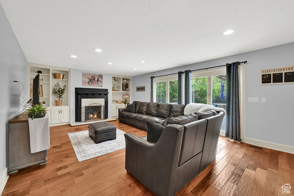 Living area featuring recessed lighting, a warm lit fireplace, and light wood finished floors