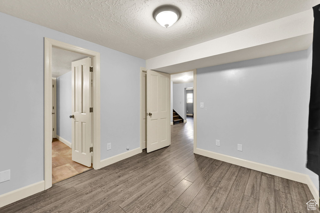 Finished below grade area with stairway, a textured ceiling, baseboards, and wood finished floors
