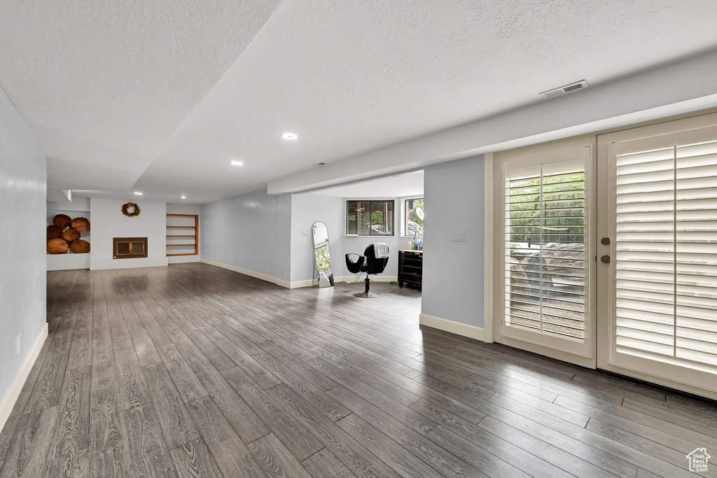 Unfurnished living room with baseboards, a textured ceiling, dark wood-style flooring, and visible vents