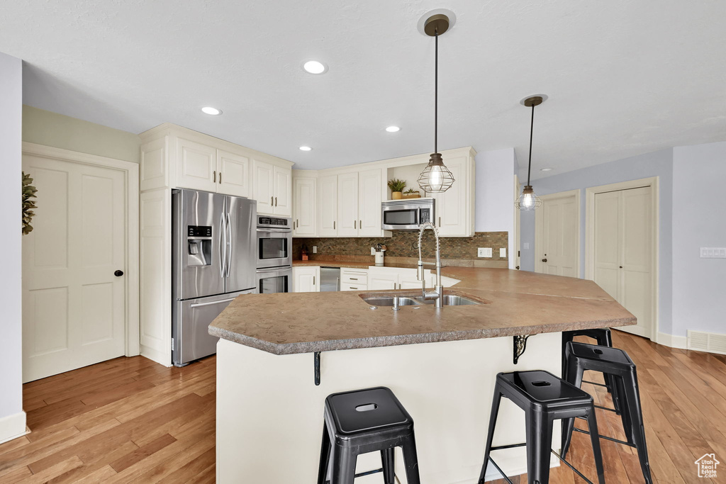 Kitchen featuring light wood-style floors, a breakfast bar area, tasteful backsplash, a sink, and appliances with stainless steel finishes