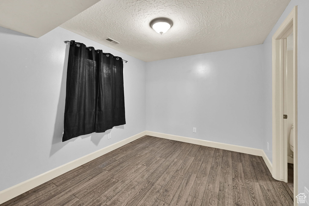 Empty room with visible vents, baseboards, a textured ceiling, and wood finished floors