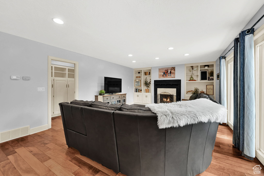 Living area with recessed lighting, a warm lit fireplace, visible vents, and light wood-style flooring