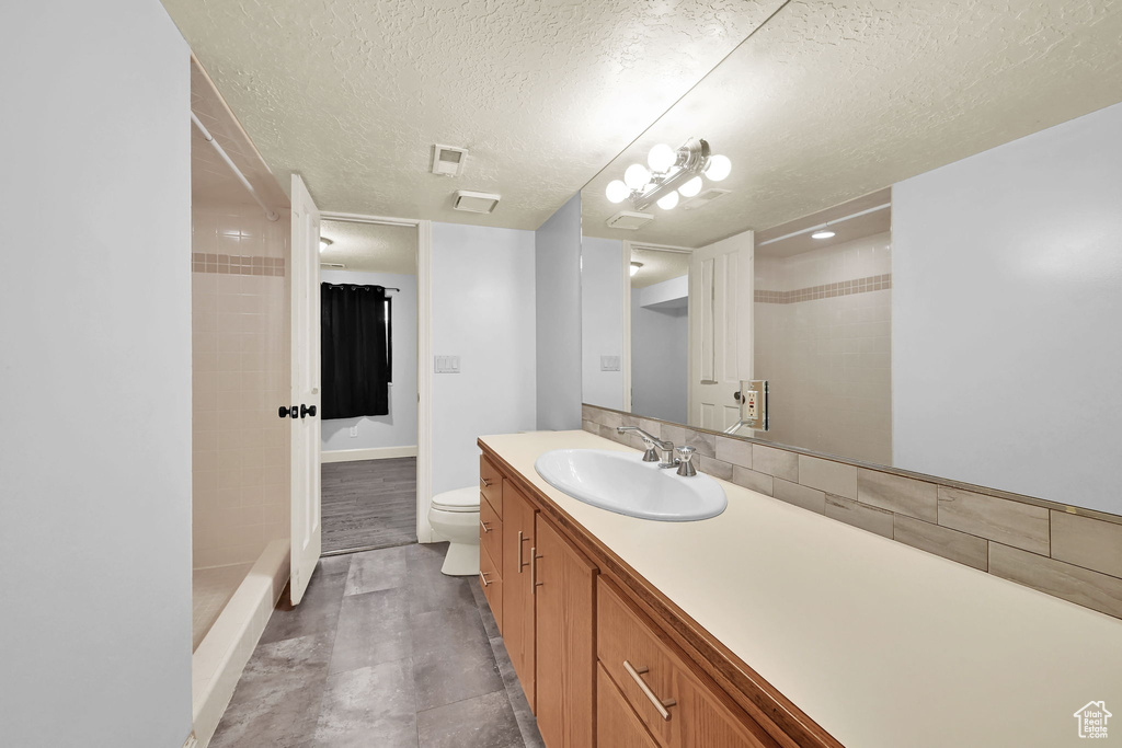 Bathroom featuring a textured ceiling, walk in shower, vanity, baseboards, and toilet