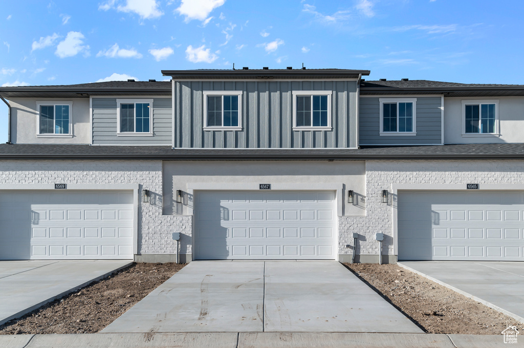 Multi unit property with a garage, stone siding, and concrete driveway