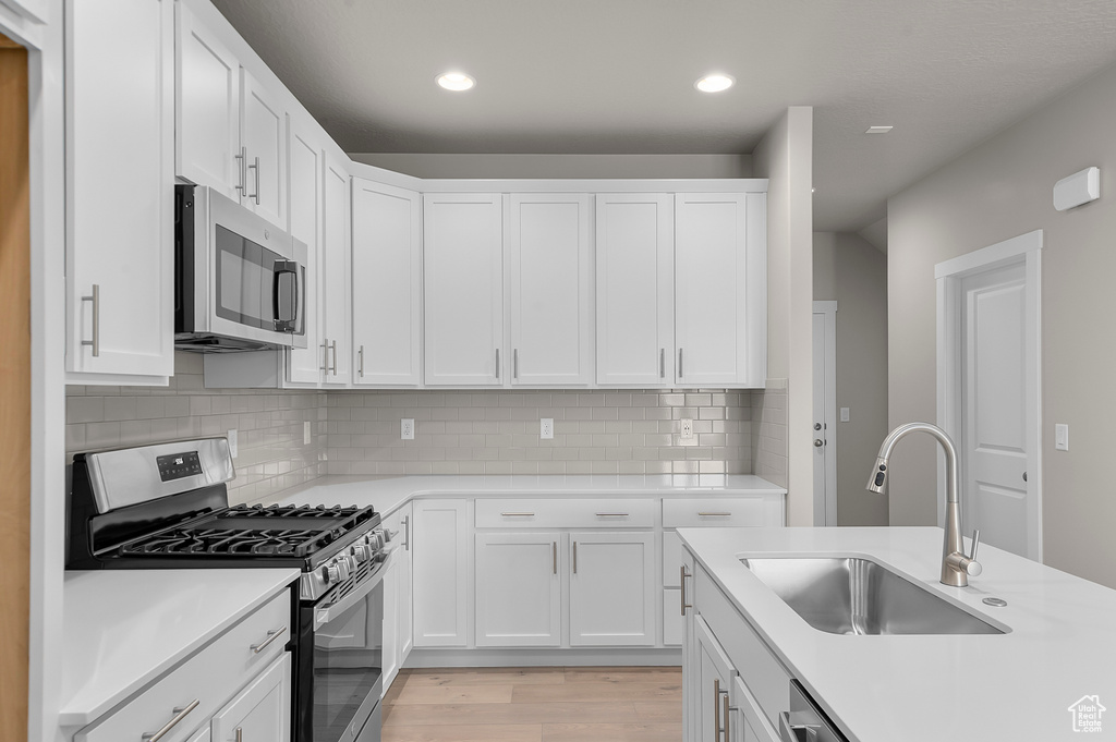 Kitchen with light wood-type flooring, light countertops, white cabinetry, a sink, and stainless steel appliances