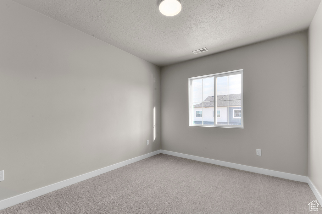 Spare room with baseboards, light carpet, a textured ceiling, and visible vents