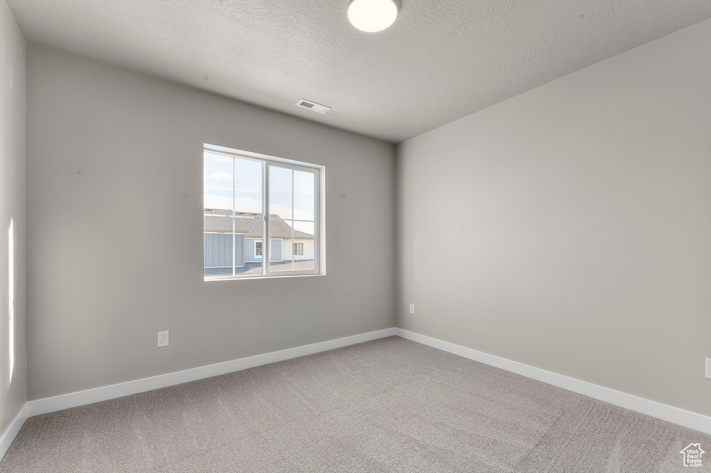 Carpeted empty room featuring a textured ceiling, baseboards, and visible vents