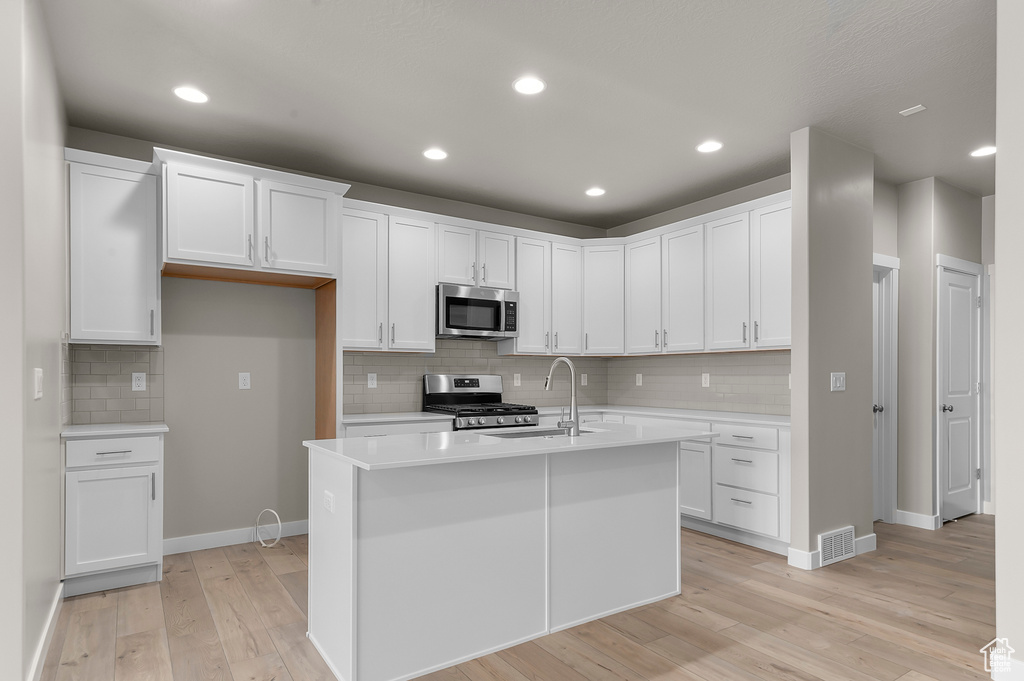 Kitchen featuring backsplash, appliances with stainless steel finishes, a sink, light countertops, and light wood finished floors