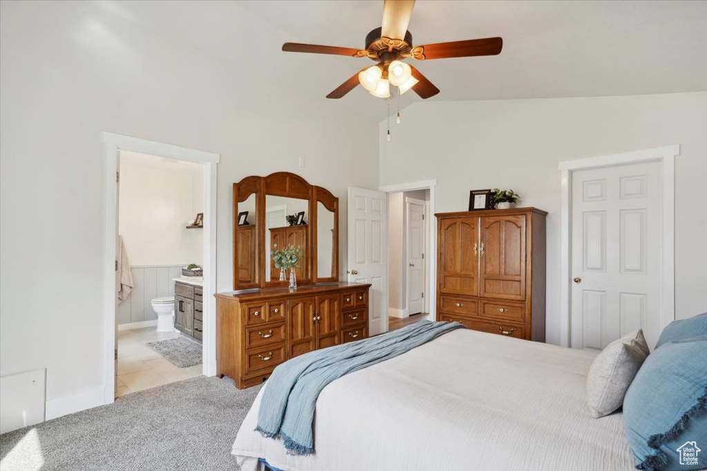 Carpeted bedroom featuring high vaulted ceiling, a ceiling fan, wainscoting, and ensuite bath
