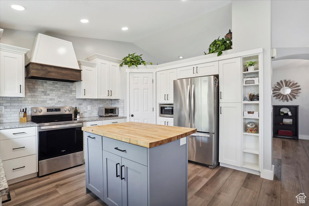 Kitchen with wooden counters, premium range hood, white cabinetry, appliances with stainless steel finishes, and vaulted ceiling