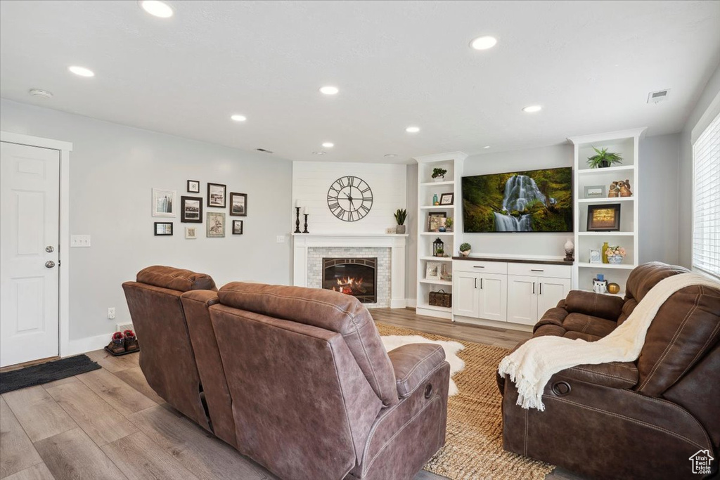 Living room with recessed lighting, a warm lit fireplace, visible vents, and light wood finished floors