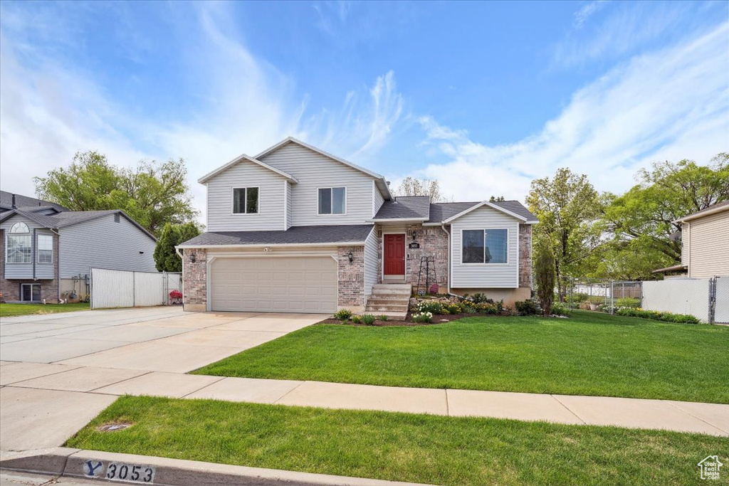 Tri-level home with fence, an attached garage, a front lawn, brick siding, and driveway