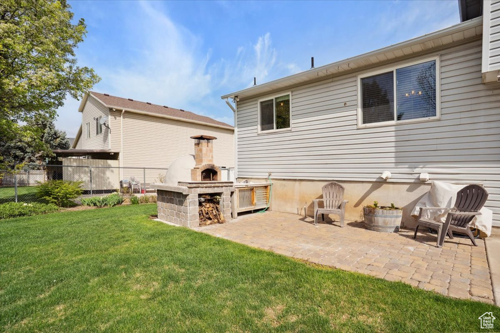 Rear view of house with fence, an outdoor fireplace, a yard, and a patio area