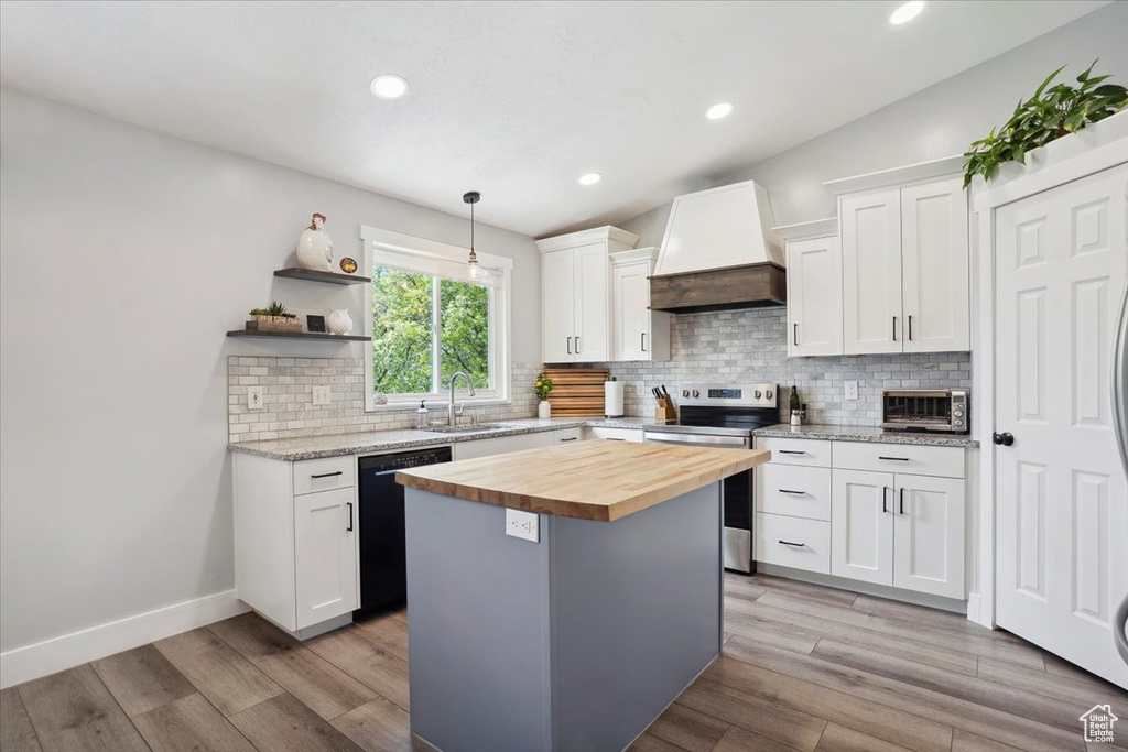 Kitchen featuring butcher block countertops, black dishwasher, custom range hood, a sink, and stainless steel range with electric cooktop