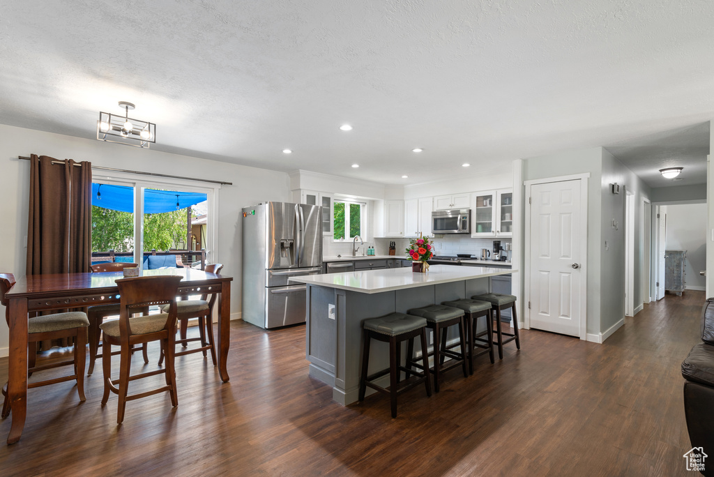 Kitchen featuring glass insert cabinets, a center island, dark wood-type flooring, white cabinetry, and stainless steel appliances