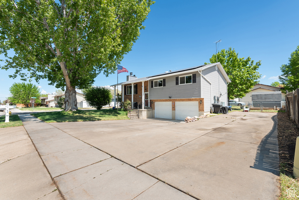 Raised ranch featuring brick siding, a garage, fence, and driveway