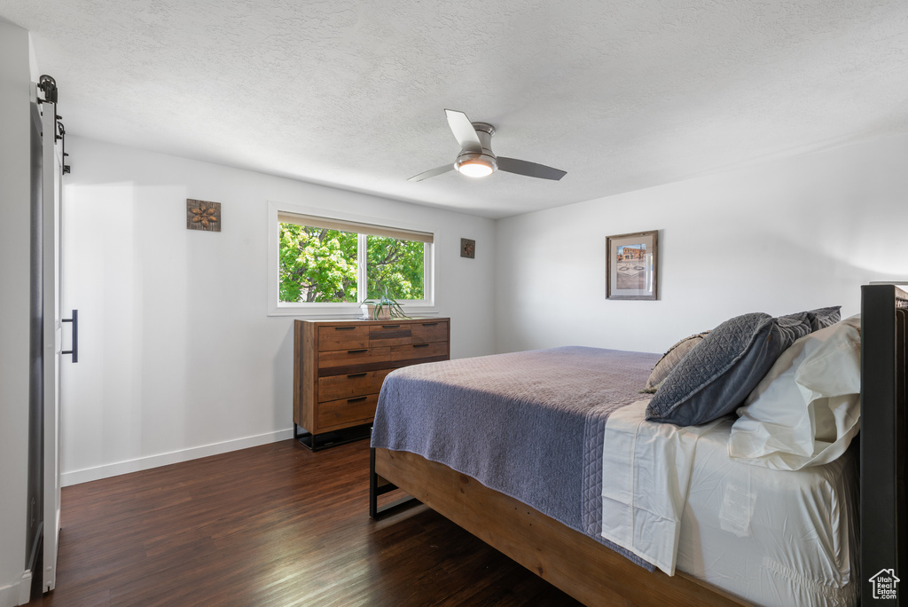 Bedroom featuring baseboards, ceiling fan, dark wood-type flooring, a barn door, and a textured ceiling