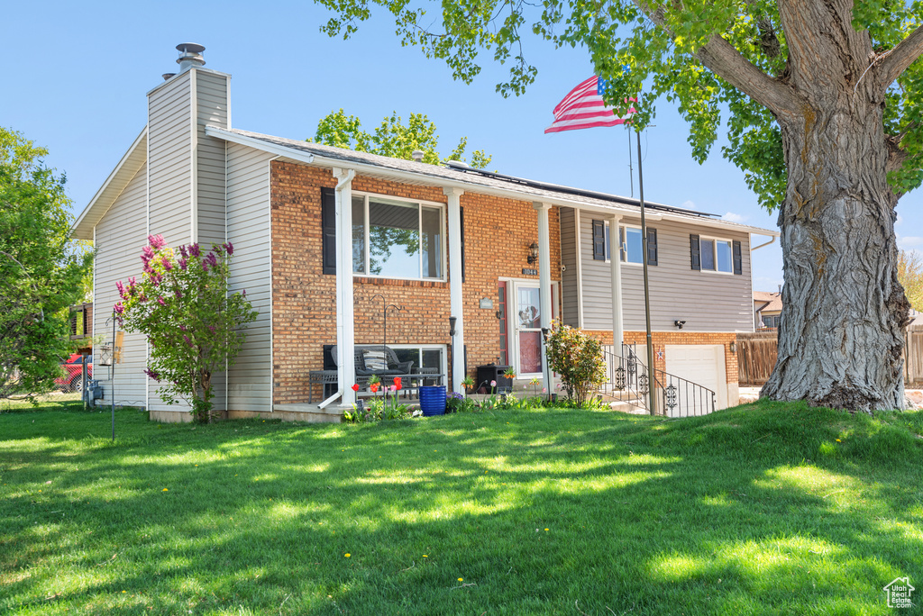 View of front of property with a chimney, an attached garage, a front lawn, and brick siding