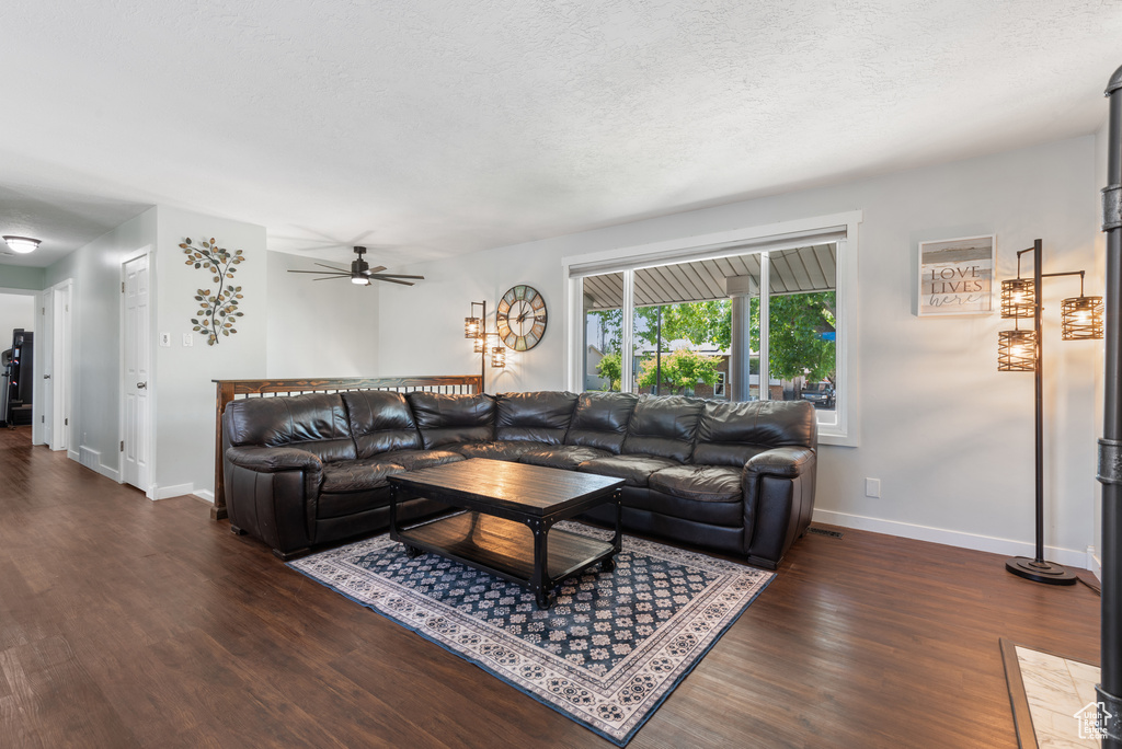 Living area featuring baseboards, a textured ceiling, dark wood finished floors, and ceiling fan