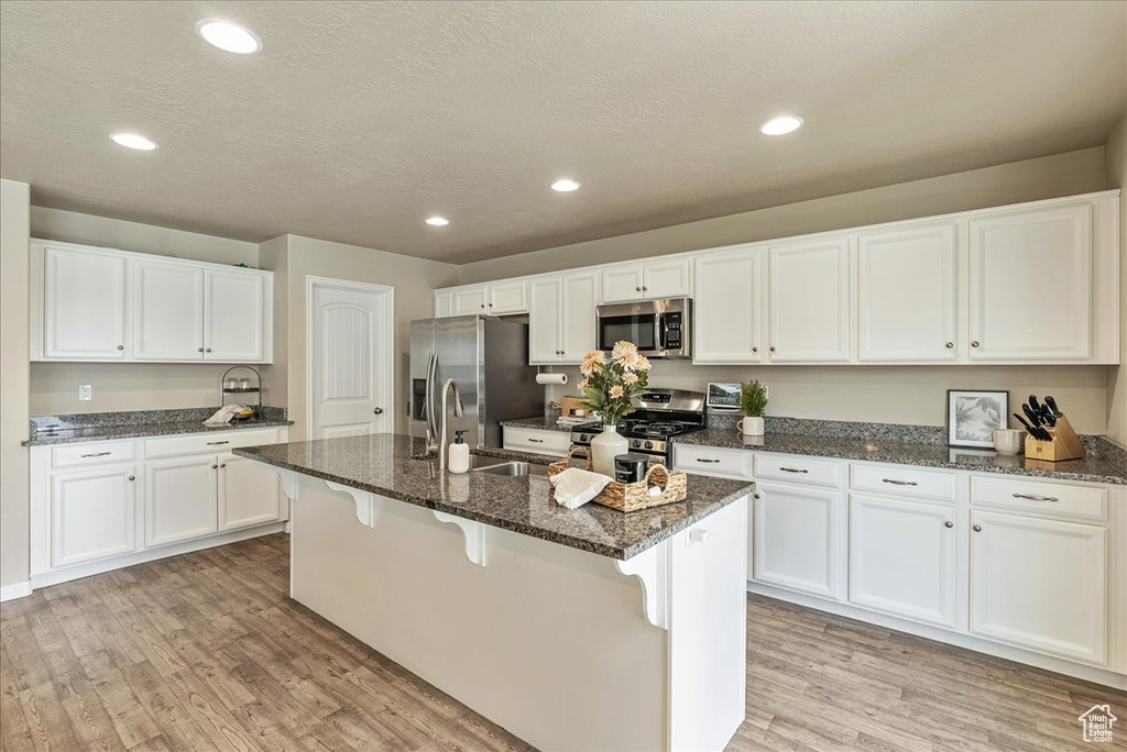 Kitchen featuring white cabinets, a sink, light wood finished floors, dark stone counters, and stainless steel appliances