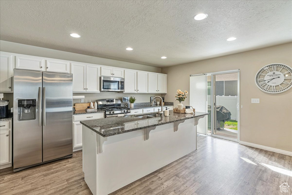 Kitchen featuring a sink, light wood finished floors, appliances with stainless steel finishes, and a breakfast bar