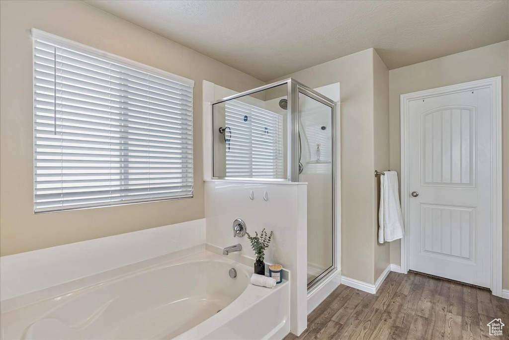 Bathroom featuring baseboards, a shower stall, wood finished floors, and a bath