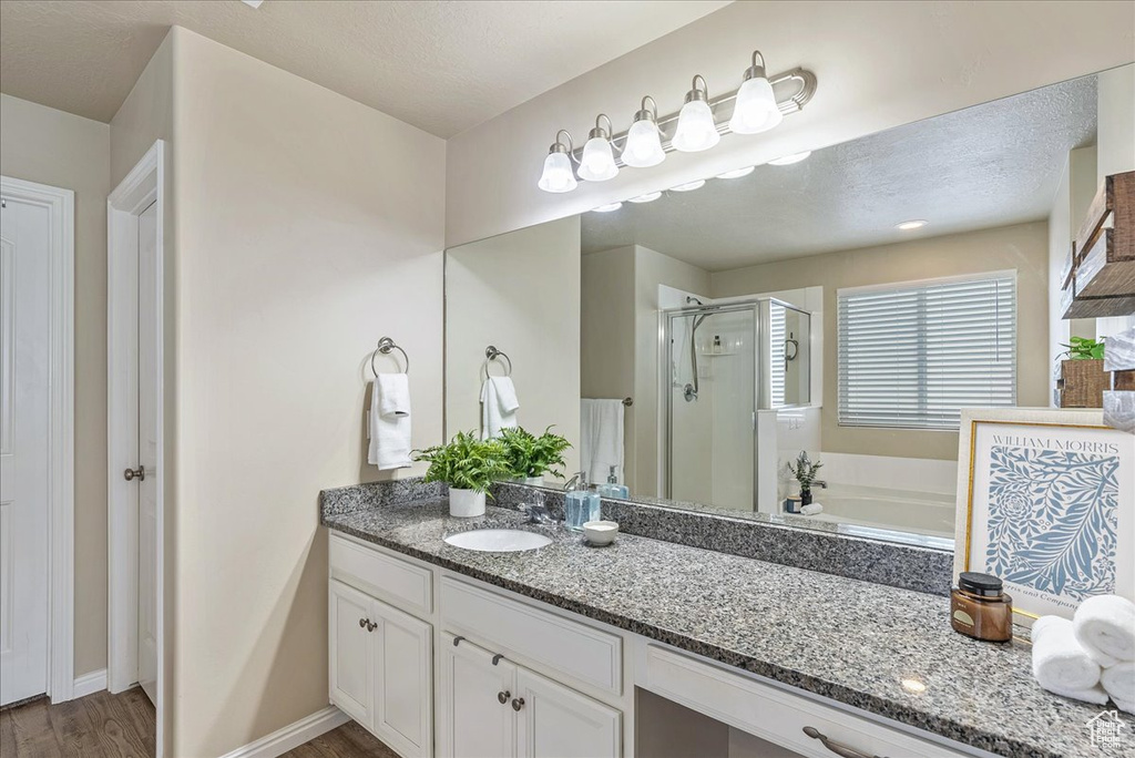 Full bath featuring vanity, baseboards, wood finished floors, a bath, and a stall shower