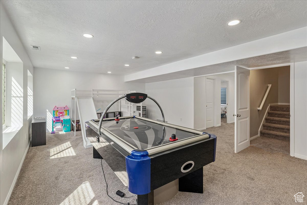Recreation room featuring baseboards, a textured ceiling, visible vents, and light carpet