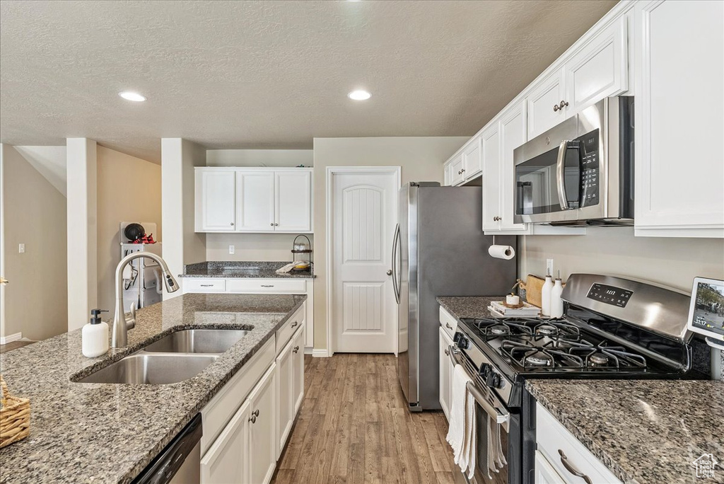 Kitchen with a sink, light wood-style flooring, stainless steel appliances, and white cabinetry