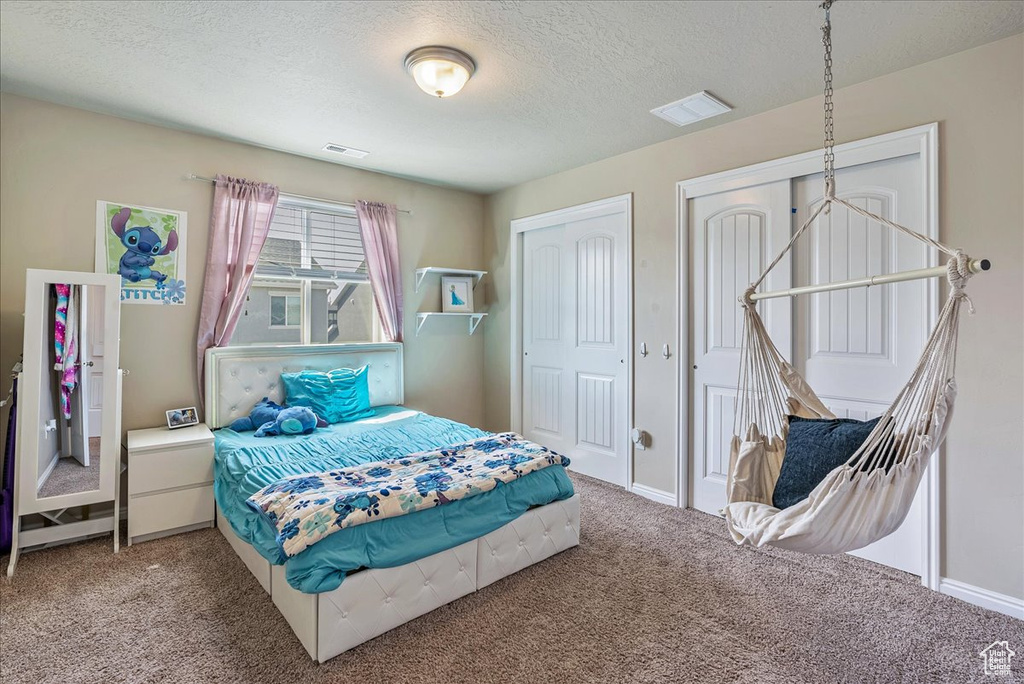 Bedroom with carpet floors, a textured ceiling, multiple closets, and visible vents