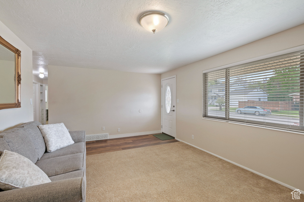 Unfurnished living room featuring baseboards, carpet flooring, a textured ceiling, and visible vents