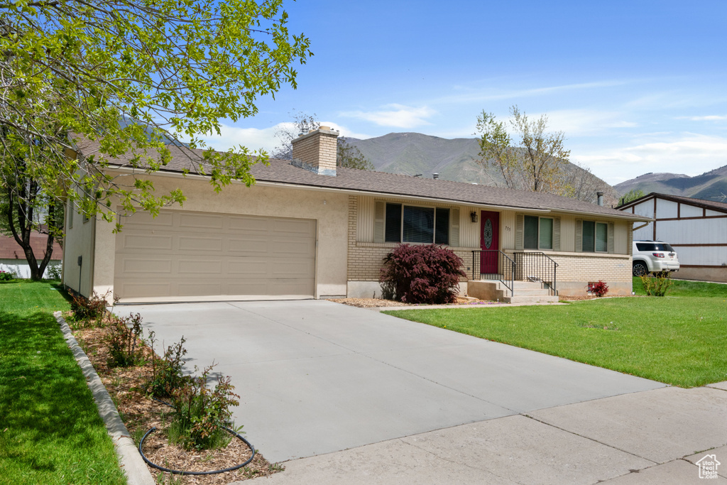 Ranch-style house with a mountain view, a chimney, an attached garage, and a front lawn