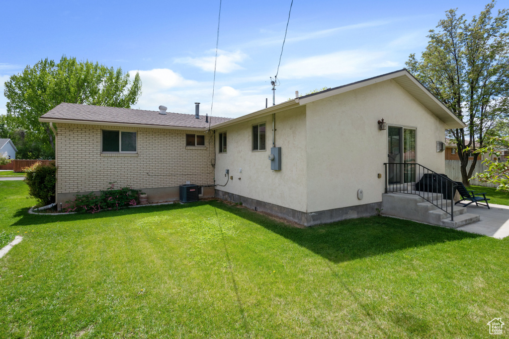 Back of house with central AC unit, stucco siding, a yard, and brick siding