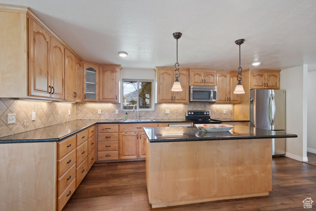 Kitchen featuring dark countertops, a sink, light brown cabinets, a center island, and stainless steel appliances