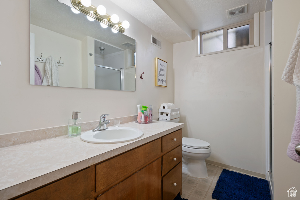 Bathroom featuring vanity, a shower with door, toilet, and visible vents