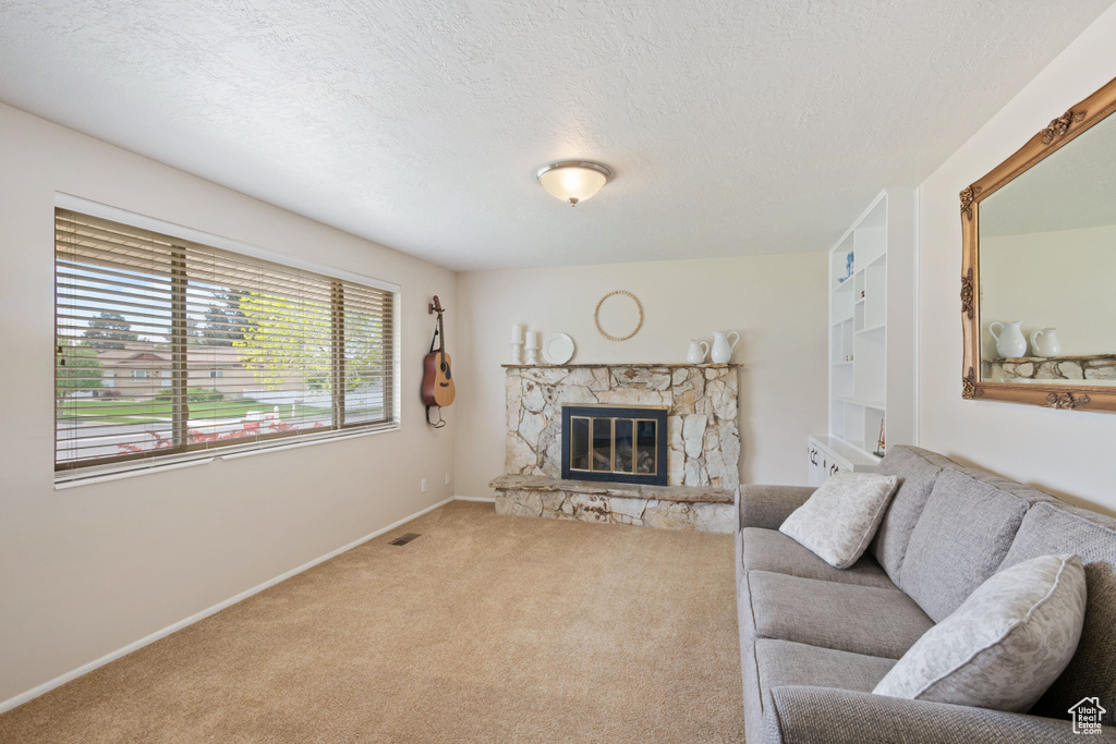 Living room with a textured ceiling, visible vents, a fireplace, baseboards, and carpet flooring
