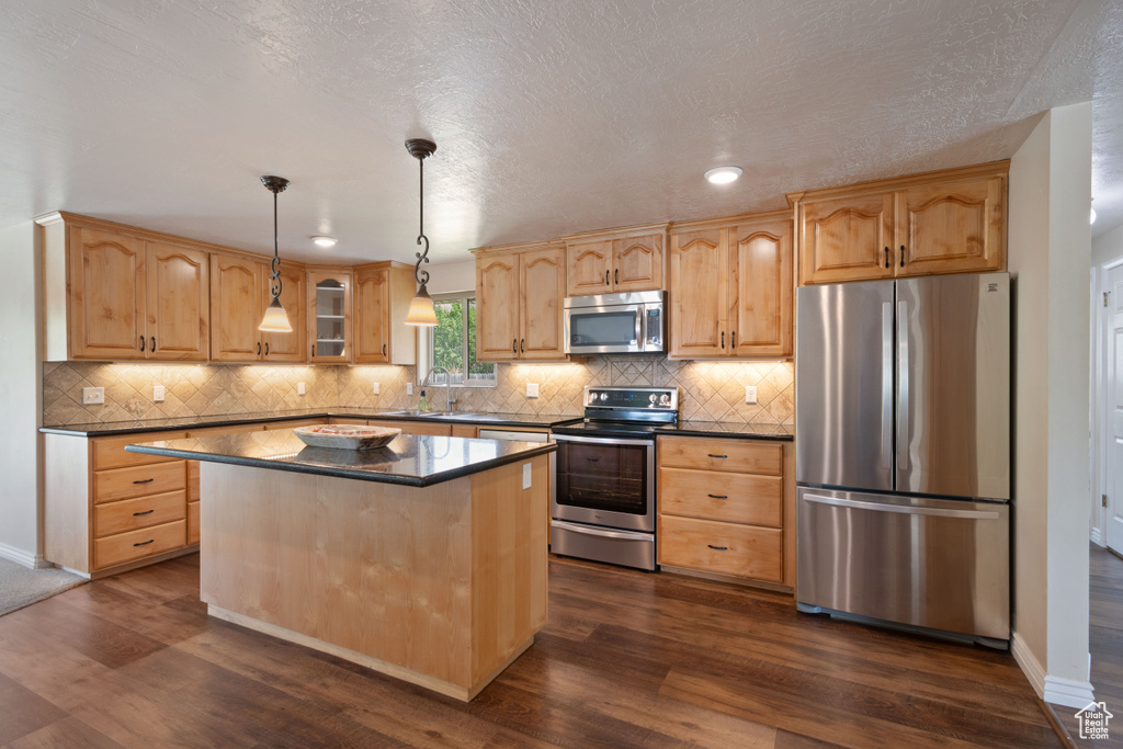 Kitchen with dark wood-style flooring, a kitchen island, dark countertops, a sink, and appliances with stainless steel finishes